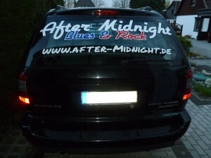 Schwarzes Auto - Heckansicht - mit Werbebeschriftung der Rockband After Midnight auf der Heckscheibe.