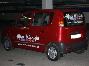 Rotes Auto mit Werbebeschriftung der Rockband After Midnight und aufgeklebten Einschusslöchern am Kotflügel.