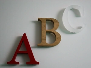 Drei gefräste Buchstaben - ein rotes A aus PE, ein braunes B aus Holz und ein transparentes C aus Acrylglas