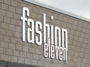 Ausschnitt einer Außenfassade mit dem Logo eines Textilhandels aus Aluminium-Farbenen Fräsbuchstaben.