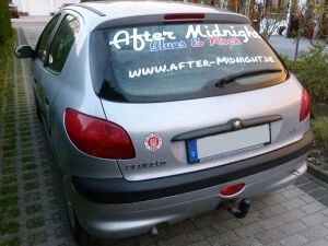 Silberner Kleinwagen mit Werbebeschriftung der Rockband After Midnight auf der Heckscheibe.