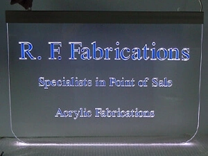 Transparentes Acrylglas-Schild mit eingefräster Schrift, die mit blauer Folie unterlegt ist und durch einen LED-Kantenstrahler zum Leuchten gebracht wird.