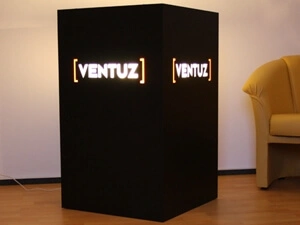 Schwarzer Würfel mit freigestellten und farbig unterlegtem Logo, beleuchtet von innen