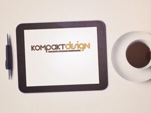 Ein Schild mit Foto als Direktdruck - Heller Hintergrund mit Kugelschreiber, Tablet auf dem das Kompaktdesign-Logo zu sehen ist und eine Tasse mit Kaffee.