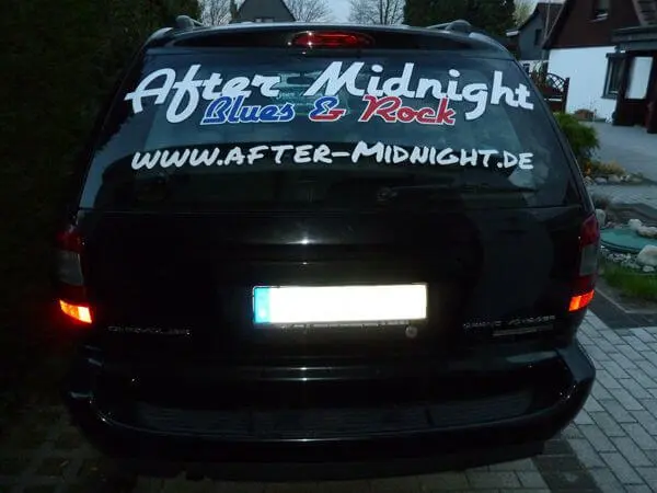 Schwarzes Auto - Heckansicht - mit Werbebeschriftung der Rockband After Midnight auf der Heckscheibe.