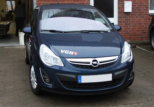 Blauer PKW - Motorhaube beschriftet mit VGH-Schriftzug in Silber und Emblem in Rot und Weiß.