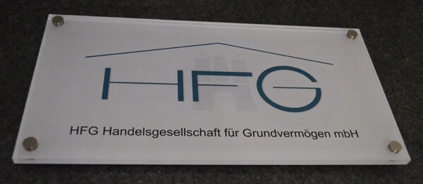 Weißes Firmenschild aus dicken Acrylglas mit Edelstahlbefestigungen in den Ecken und blauen Schriftzug "HFG - Handelsgesellschaft für Grundvermögen mbH".