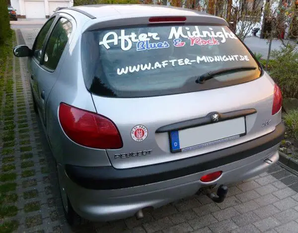Silberner Kleinwagen mit Werbebeschriftung der Rockband After Midnight auf der Heckscheibe.