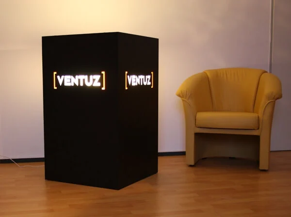 Schwarzer Würfel mit freigestellten und farbig unterlegtem Logo, beleuchtet von innen