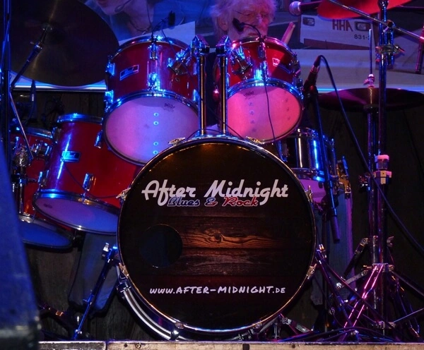 Folienbeschriftete Base-Drum - Holz-Hintergrund und Rockband-Logo - am Schlagzeug.